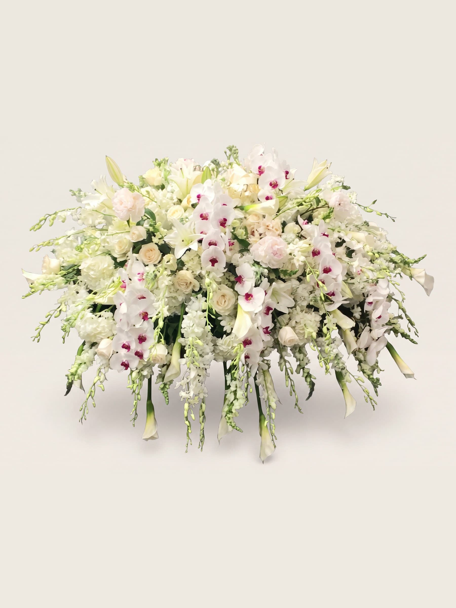 Wide all-white casket spray of orchids, garden roses, gladiolus, and calla lilies