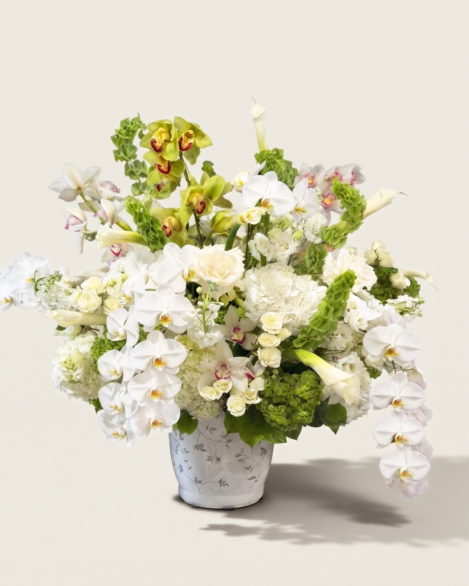 Grand white and green arrangement of orchids, calla lilies, roses and hydrangea in a hand-painted ceramic urn